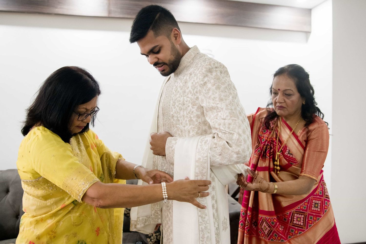 Family members help prepare traditional Indian wedding attire in a modern living room setting.