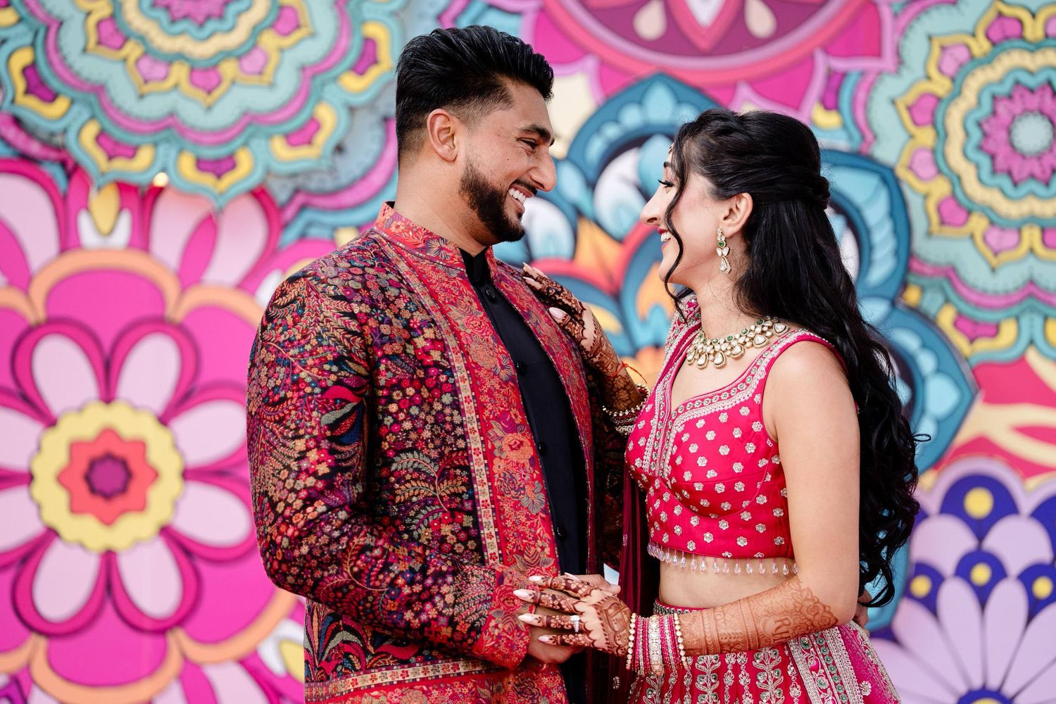 Couple in traditional Indian wedding attire embracing against a vibrant floral backdrop.