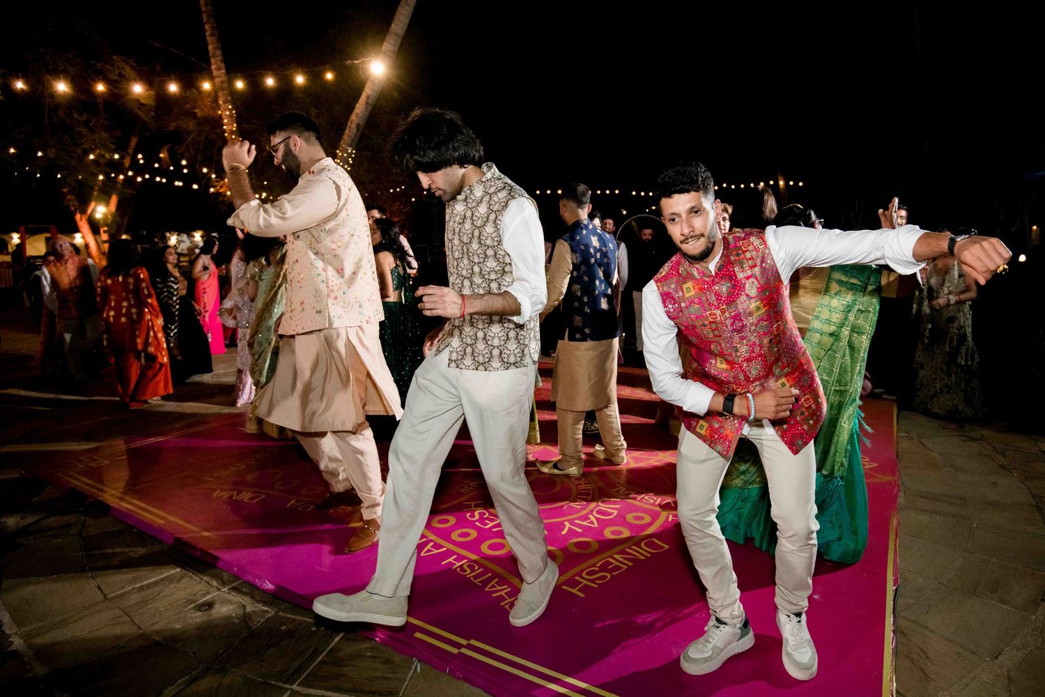 Wedding guests dance and celebrate on a pink-lit dance floor during an evening outdoor reception.