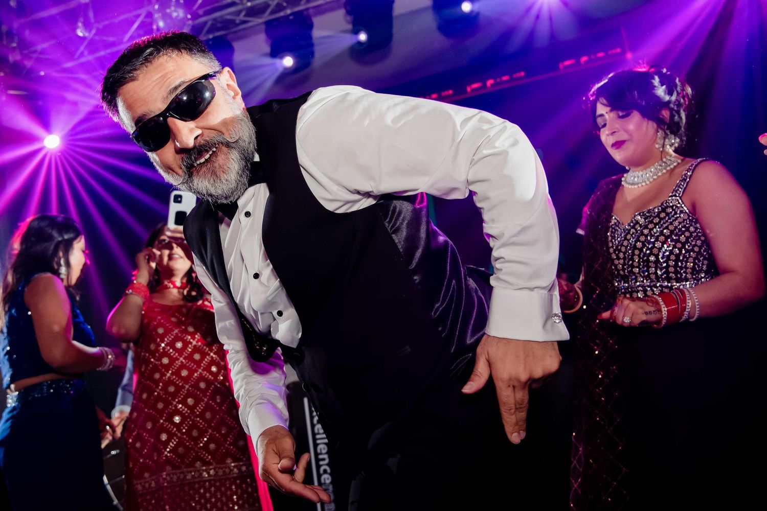 A person in formal attire strikes a playful pose on a purple-lit dance floor.