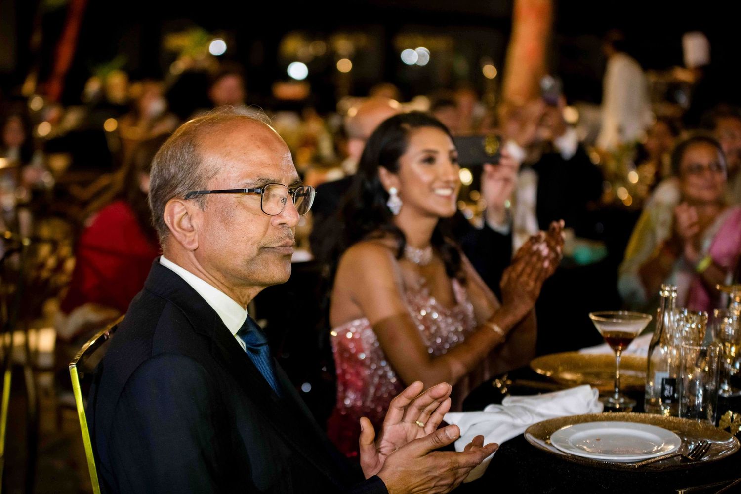 Evening banquet guests applaud during an elegant dinner event with lit candles and formal place settings.