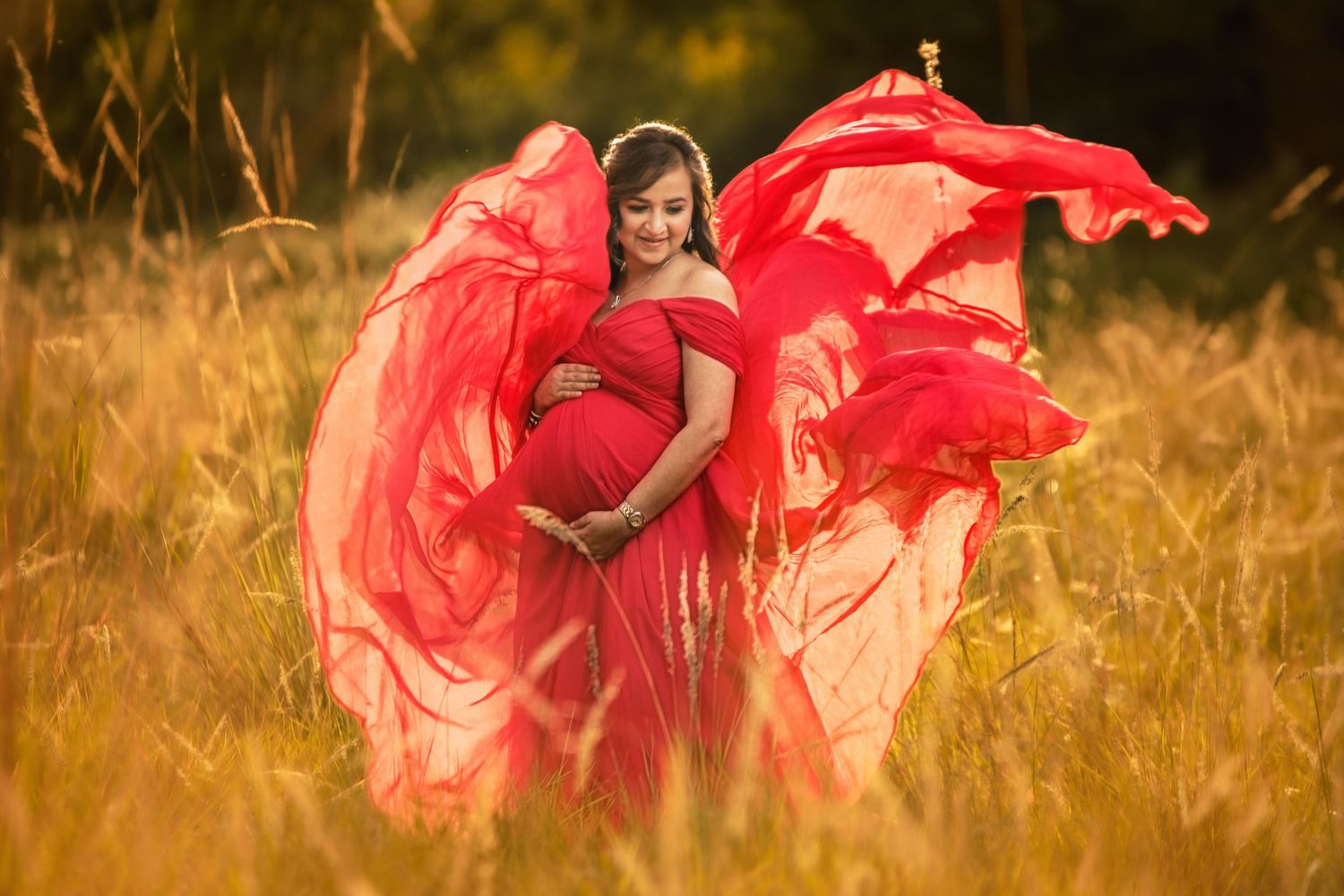 Woman in flowing red dress poses gracefully in golden field during sunset.