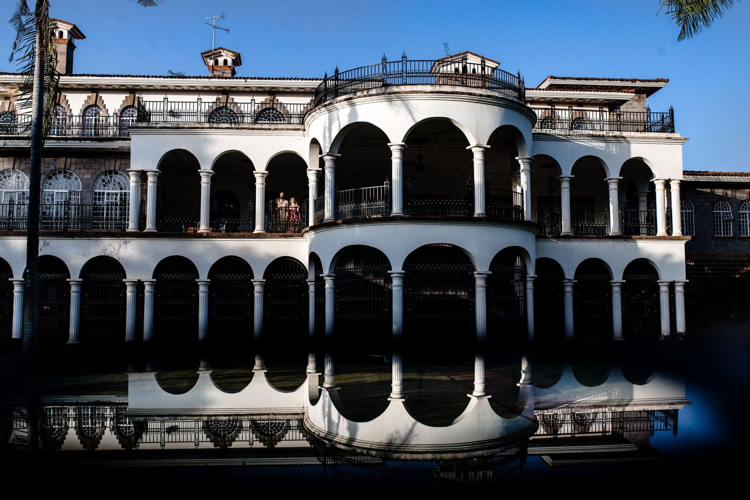 Historic white colonial building with arches reflecting perfectly in still water.