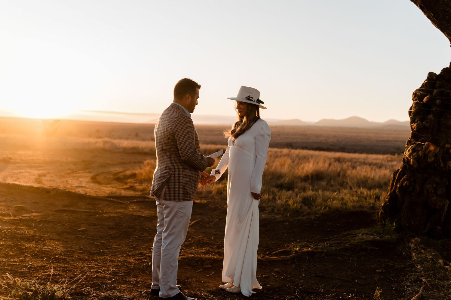A couple shares an intimate moment in white attire during golden hour in a desert landscape.