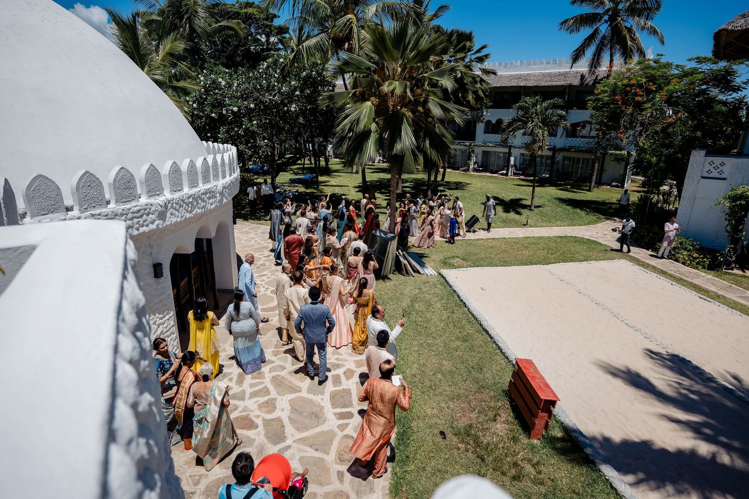 Celebrants gather outside a white domed building surrounded by palm trees and tropical landscaping.