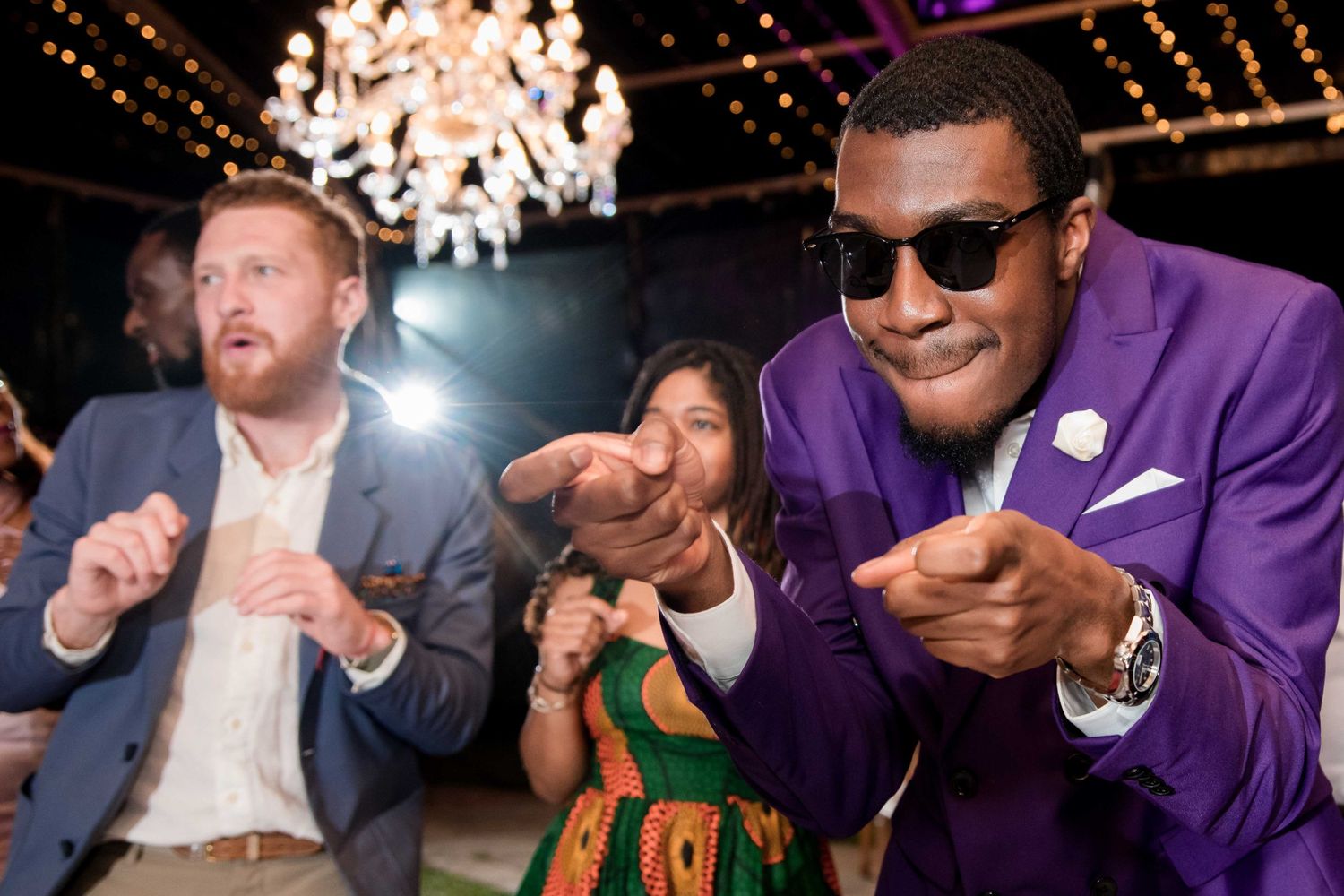 Wedding guests showing off dance moves under a crystal chandelier at a lively reception.