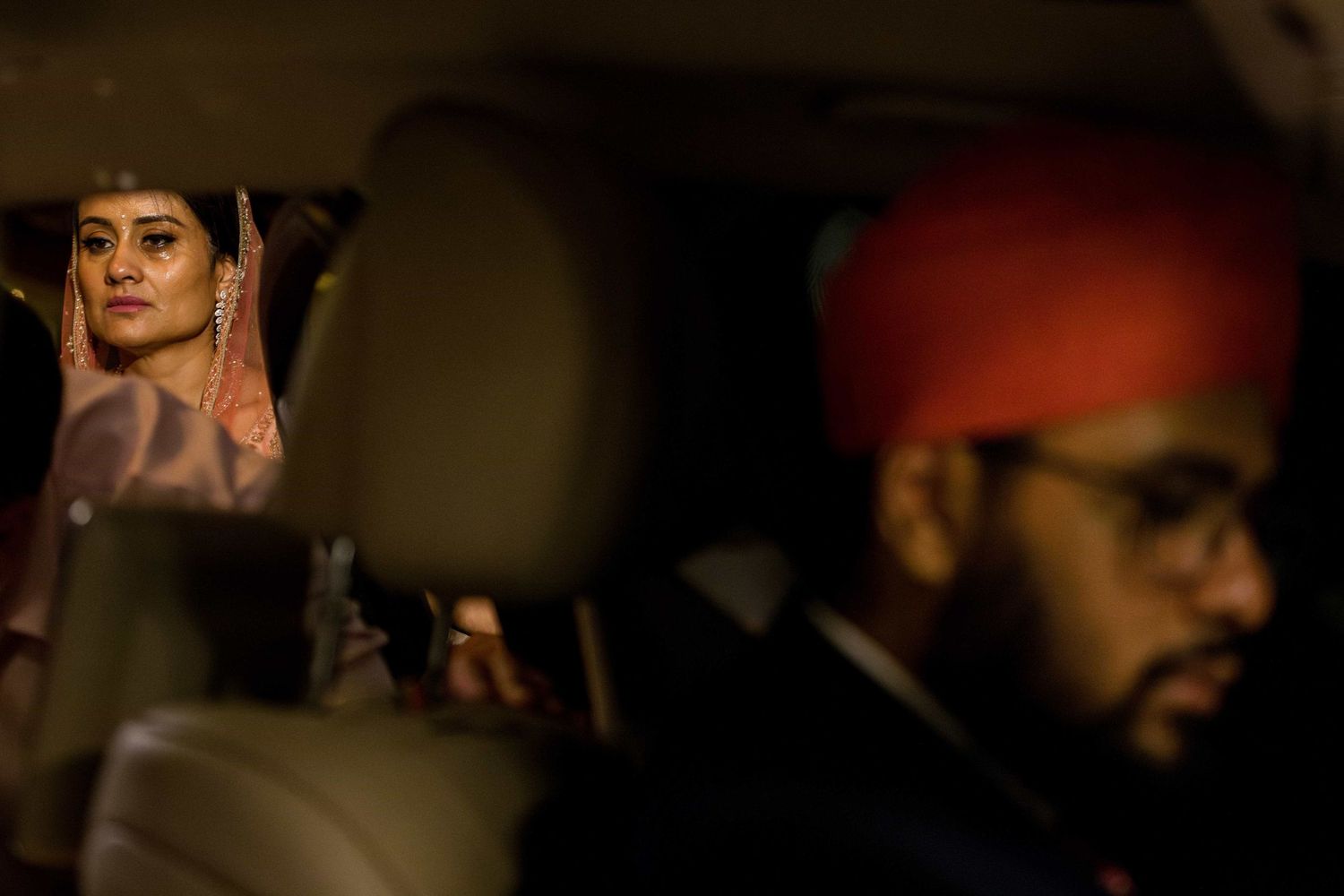 Two passengers sitting in a car interior illuminated by warm lighting during an evening event.