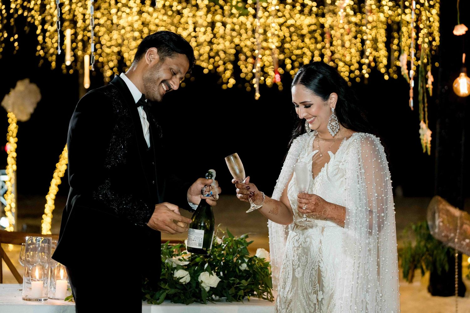 An elegant evening wedding reception with hanging string lights creating a warm golden ambiance.
