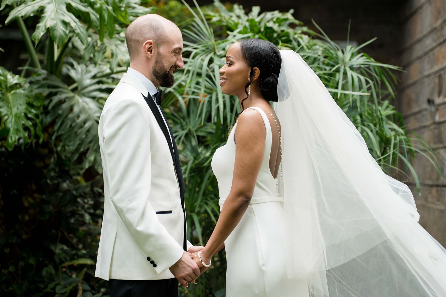 A romantic wedding couple shares joyful moments together in a lush tropical garden setting with palm trees.