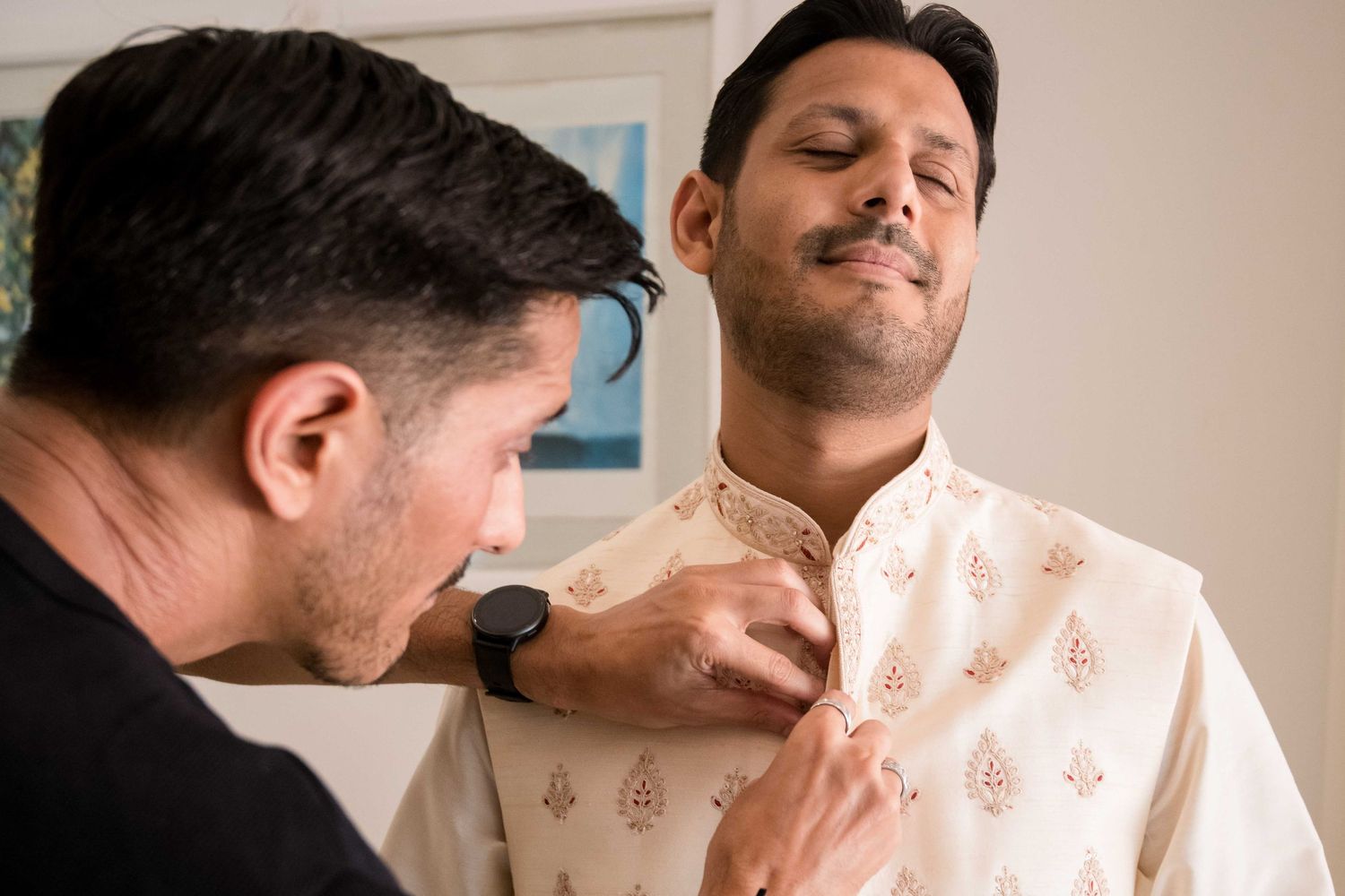 Someone helps adjust a traditional patterned kurta shirt during a formal dressing preparation.