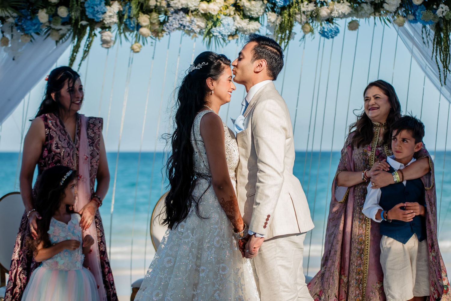 Romantic beach wedding scene with white floral arch and ocean backdrop.