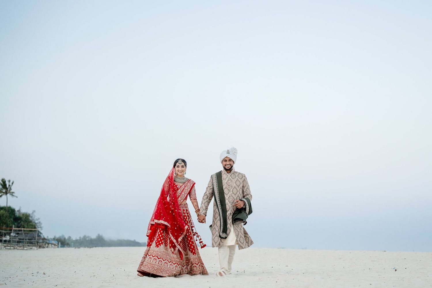 A couple walks along a sandy beach with a cloudy sky in the background.