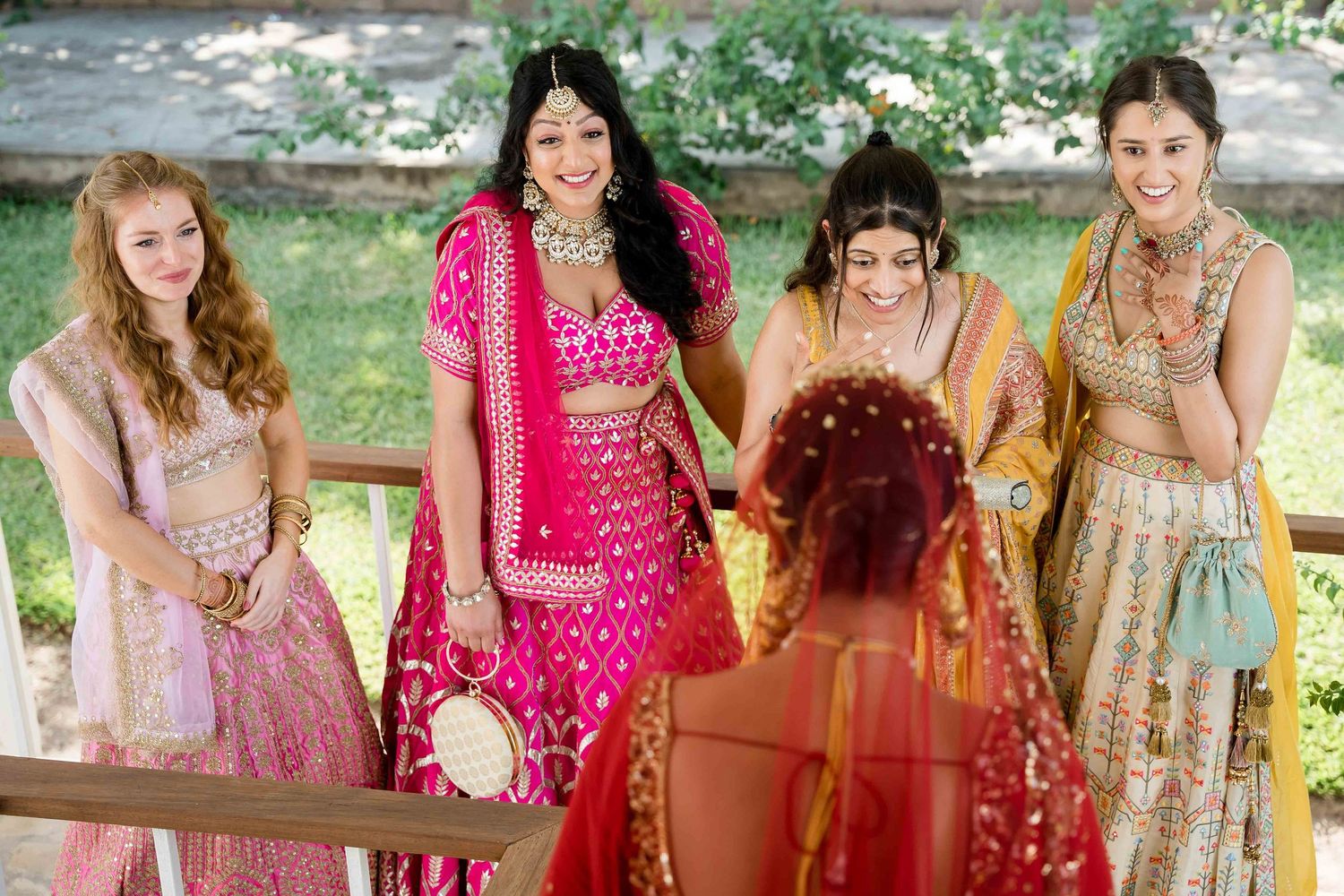 Group wearing colorful traditional Indian wedding attire poses together in an outdoor garden setting.