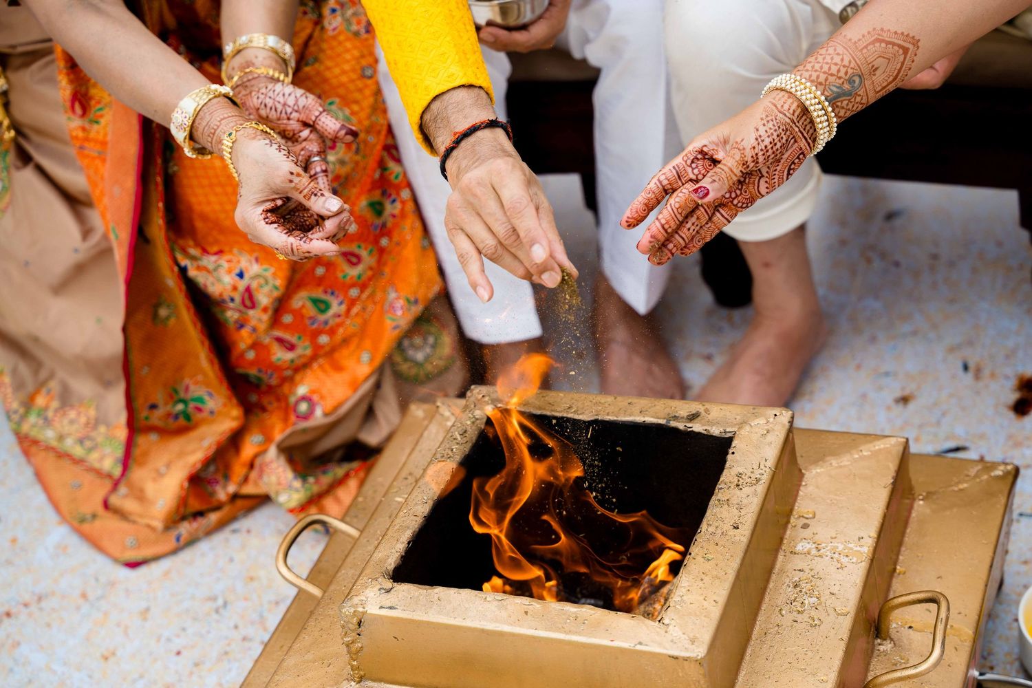 Hands adorned with henna designs are shown preparing and cooking traditional Indian food in a kitchen setting.