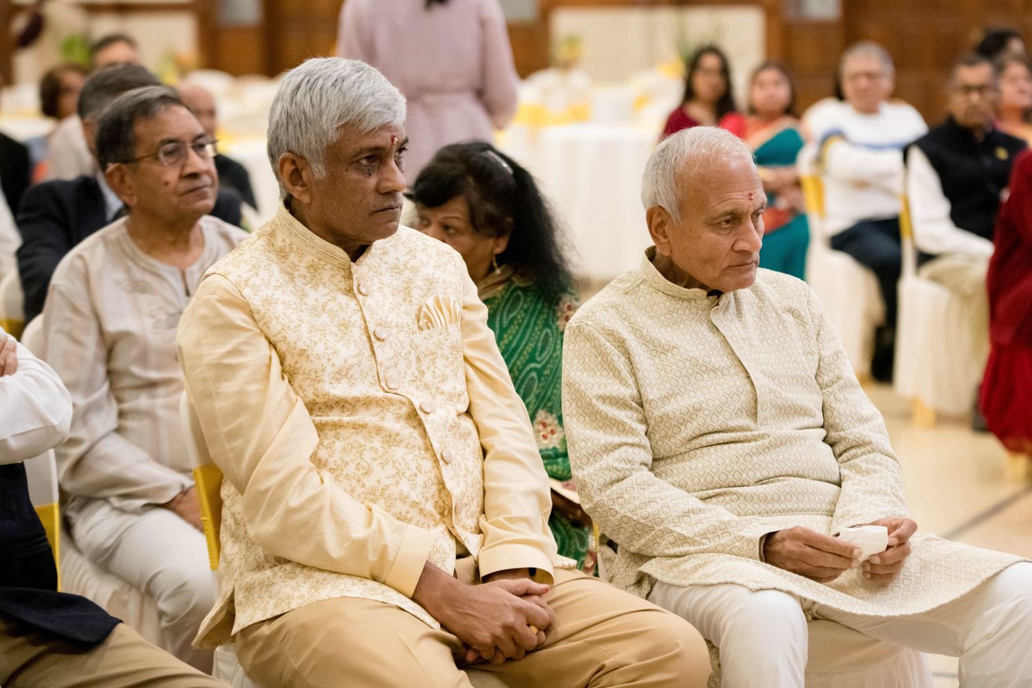 Guests in elegant cream and gold Indian formal wear seated during a ceremony.
