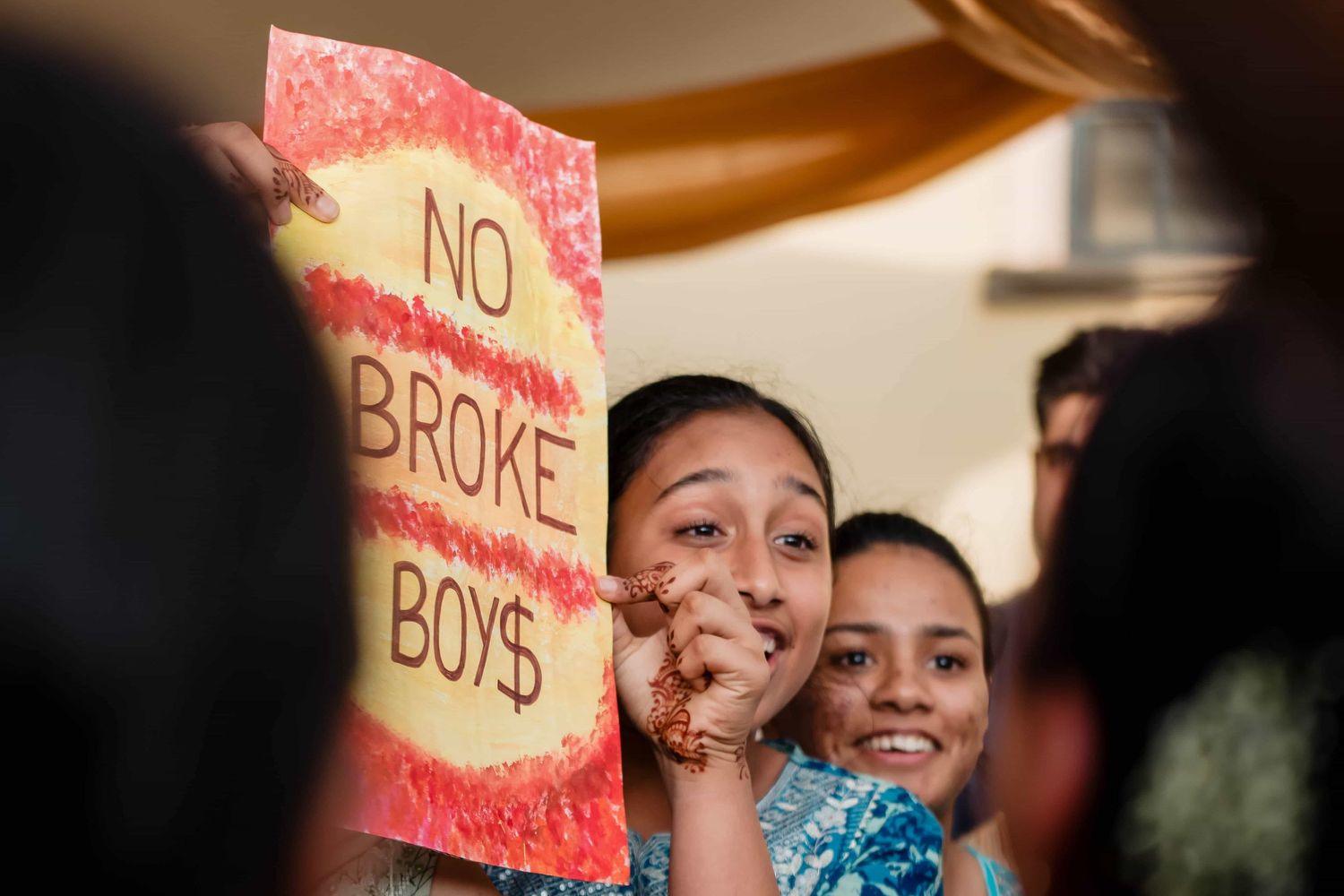 Playful wedding guests holding humorous 'No Broke Boys' sign during celebration.