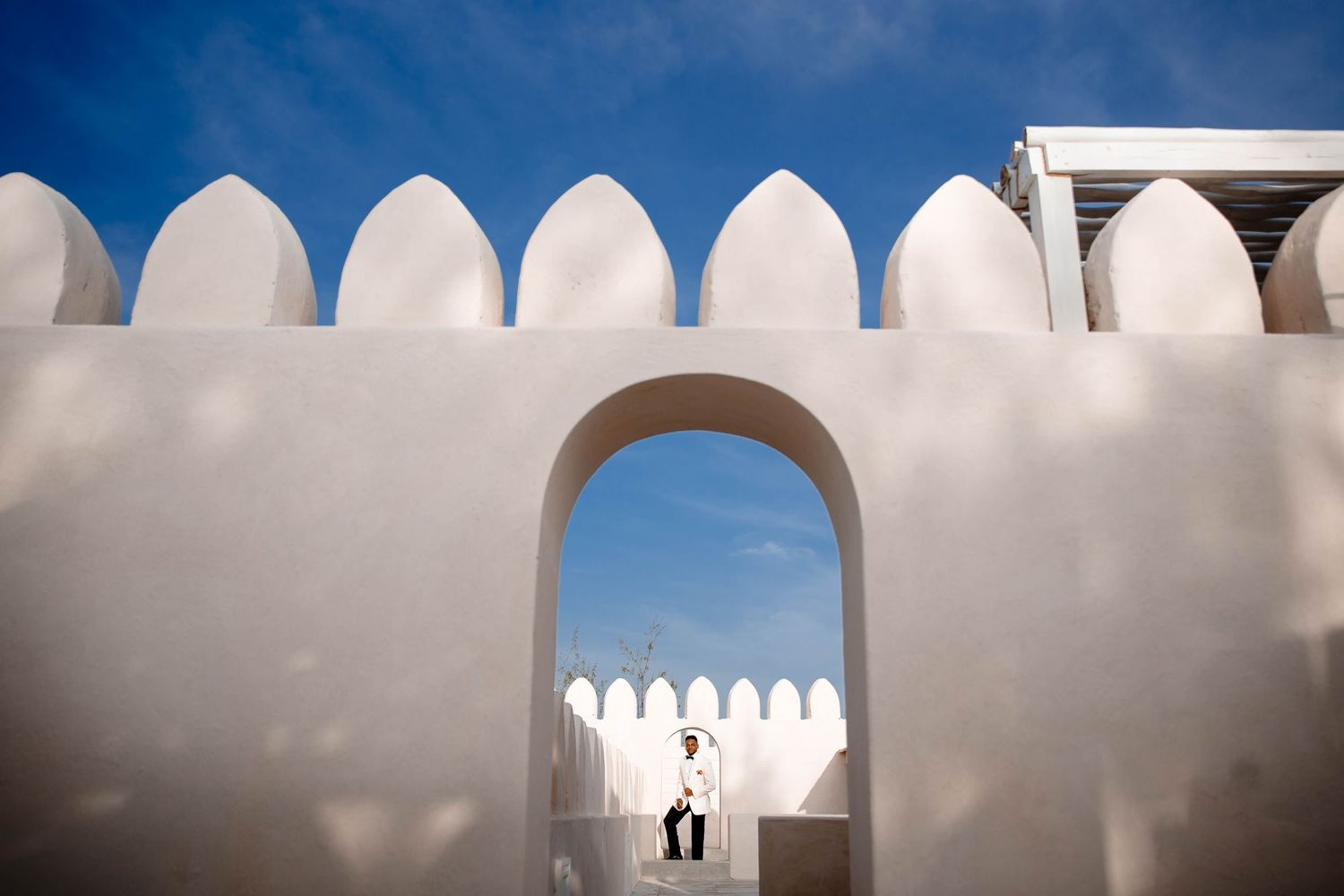 A series of white arched architectural elements against a blue sky creating a minimalist geometric pattern.