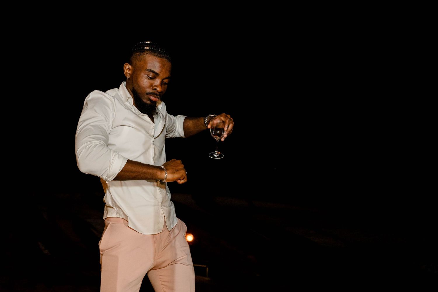 A person in a white shirt and khaki pants dances with expressive movement against a dark background.