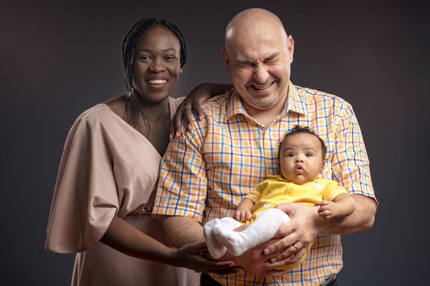 Family portrait series showing joyful moments between parents and baby against dark studio backdrop.