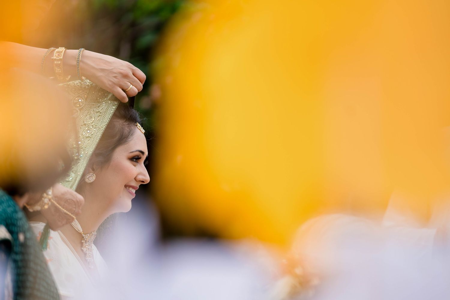 A bride in white veil is photographed against a blurred orange and white background during a wedding ceremony.