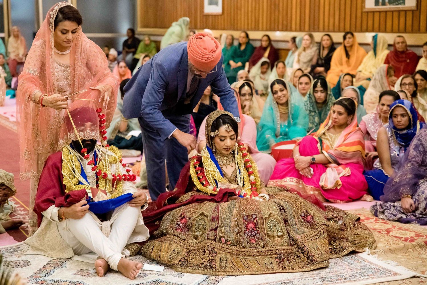 Colorful traditional Sikh wedding ceremony with attendees in vibrant attire seated on floor.