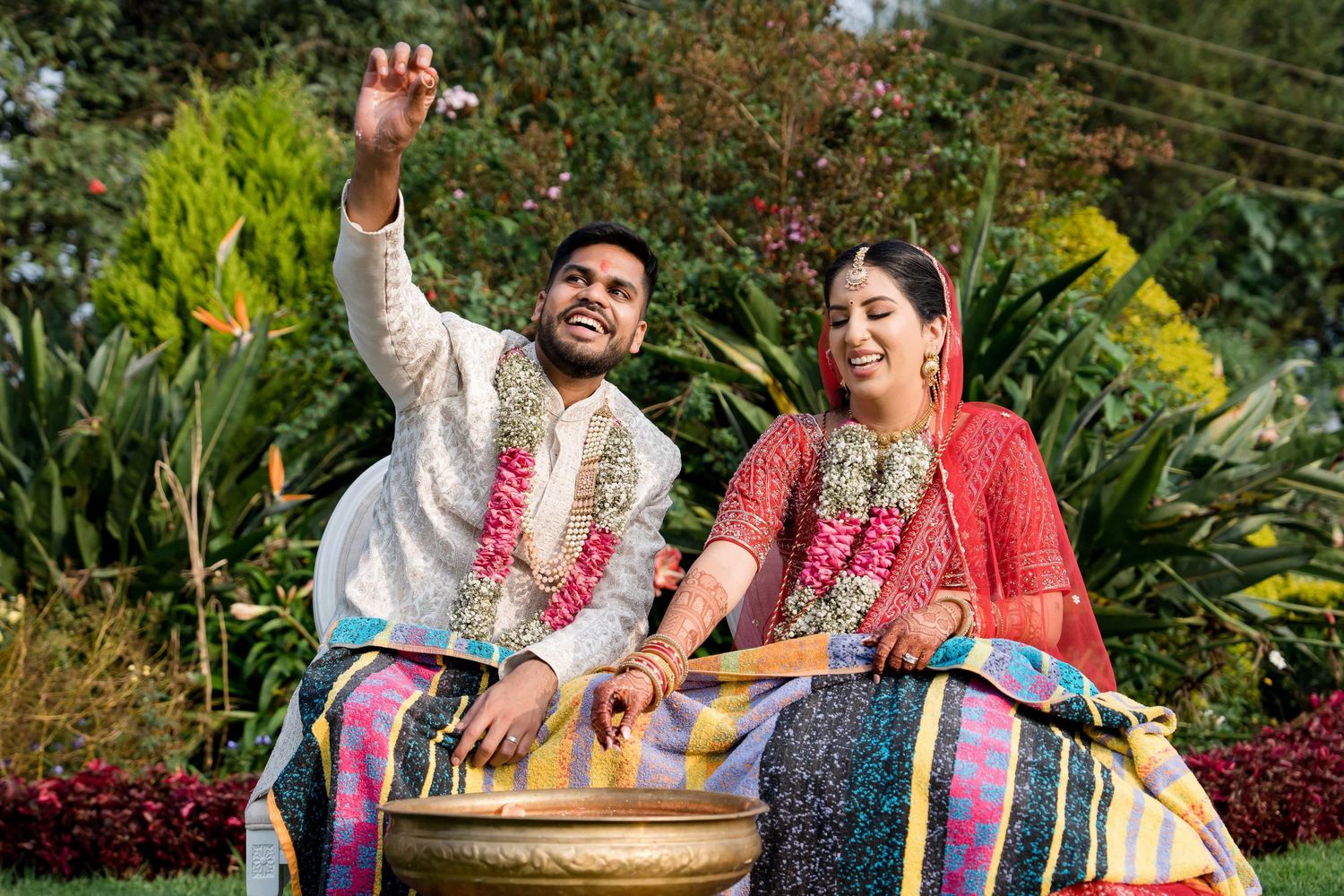 Couple in traditional Indian wedding attire celebrating outdoors in a garden setting.