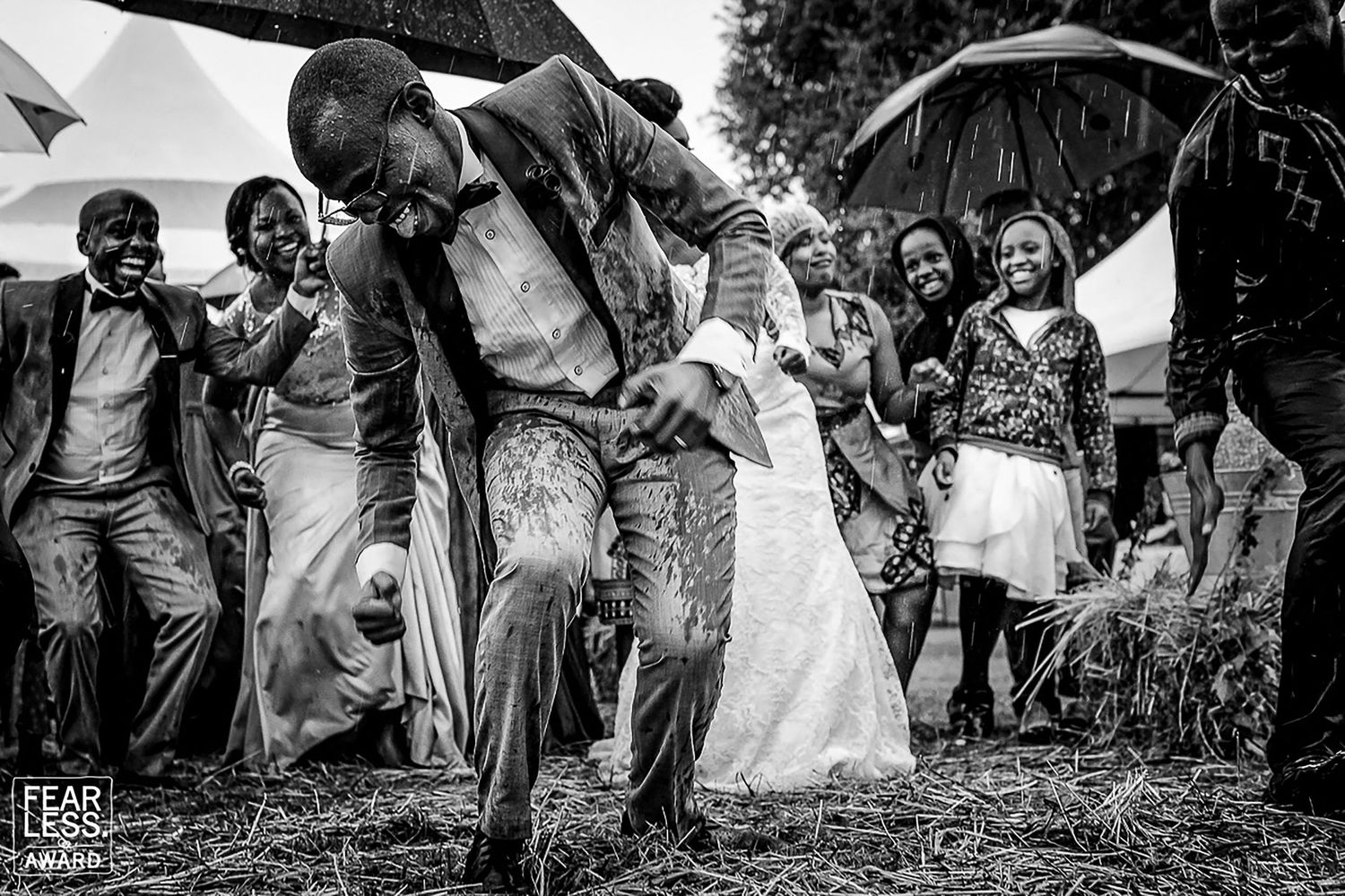 Wedding party members playfully reach down to touch the ground in a synchronized group pose outdoors.