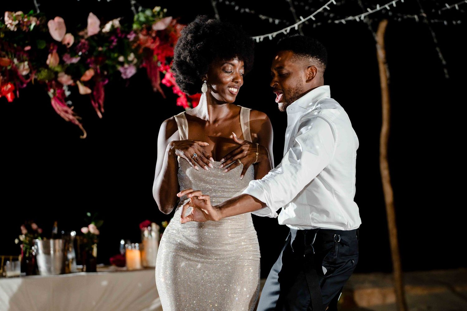 A couple shares a romantic dance moment at an evening wedding reception with twinkling lights in the background.