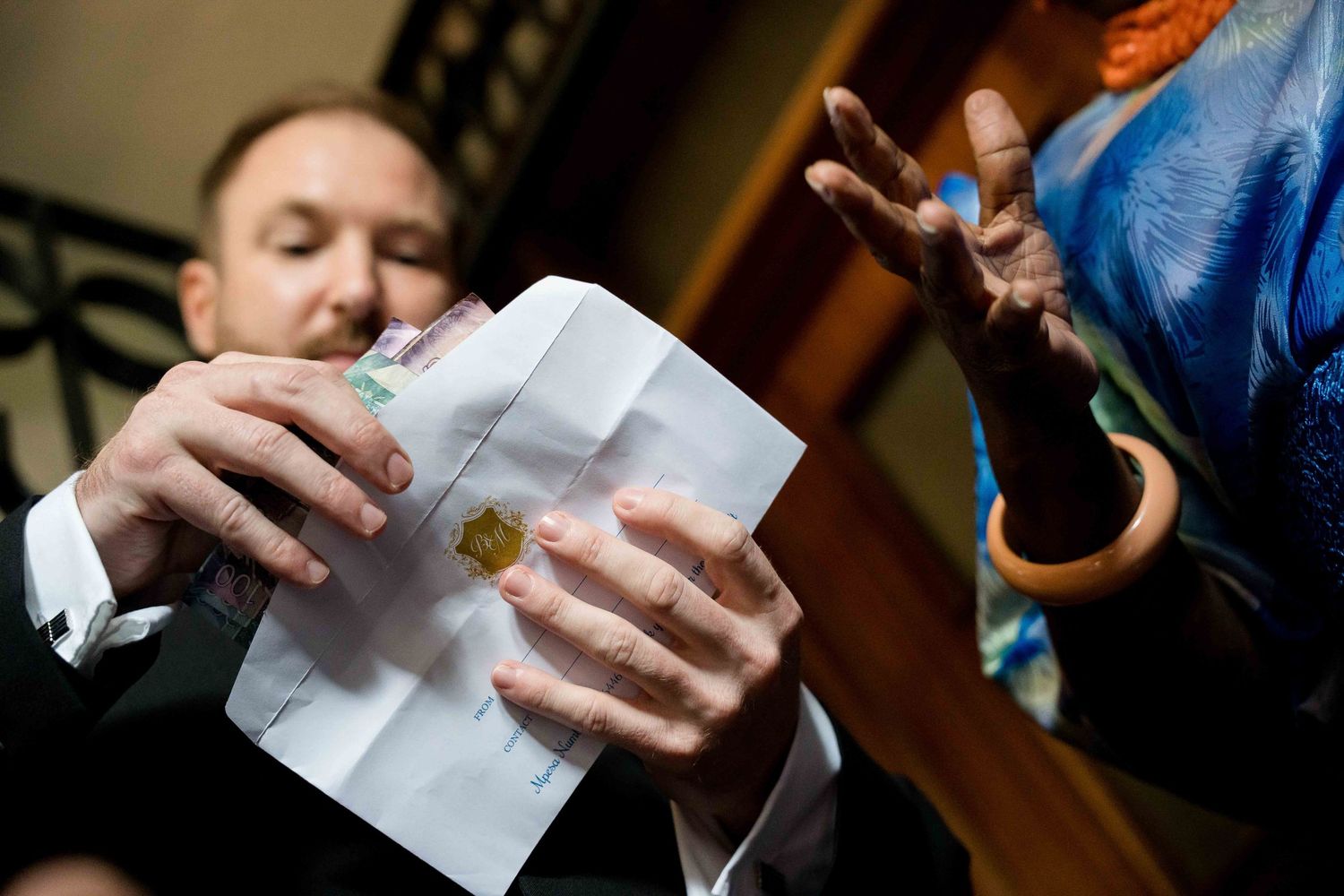 Close-up shot of hands opening an envelope during a formal gathering.