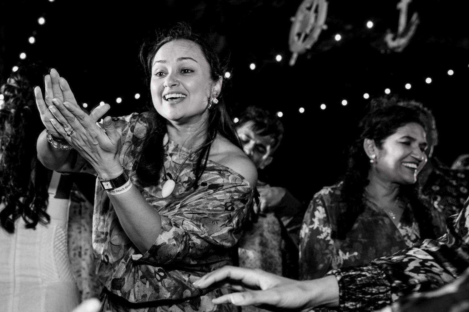 People applaud and celebrate at a nighttime event with string lights overhead in this black and white photograph.