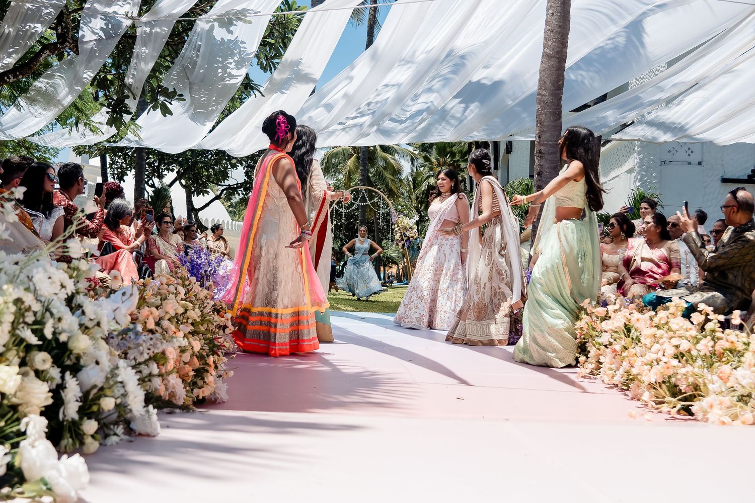 Elegant outdoor wedding setup with flowing fabric canopy and floral decorations along pink walkway.
