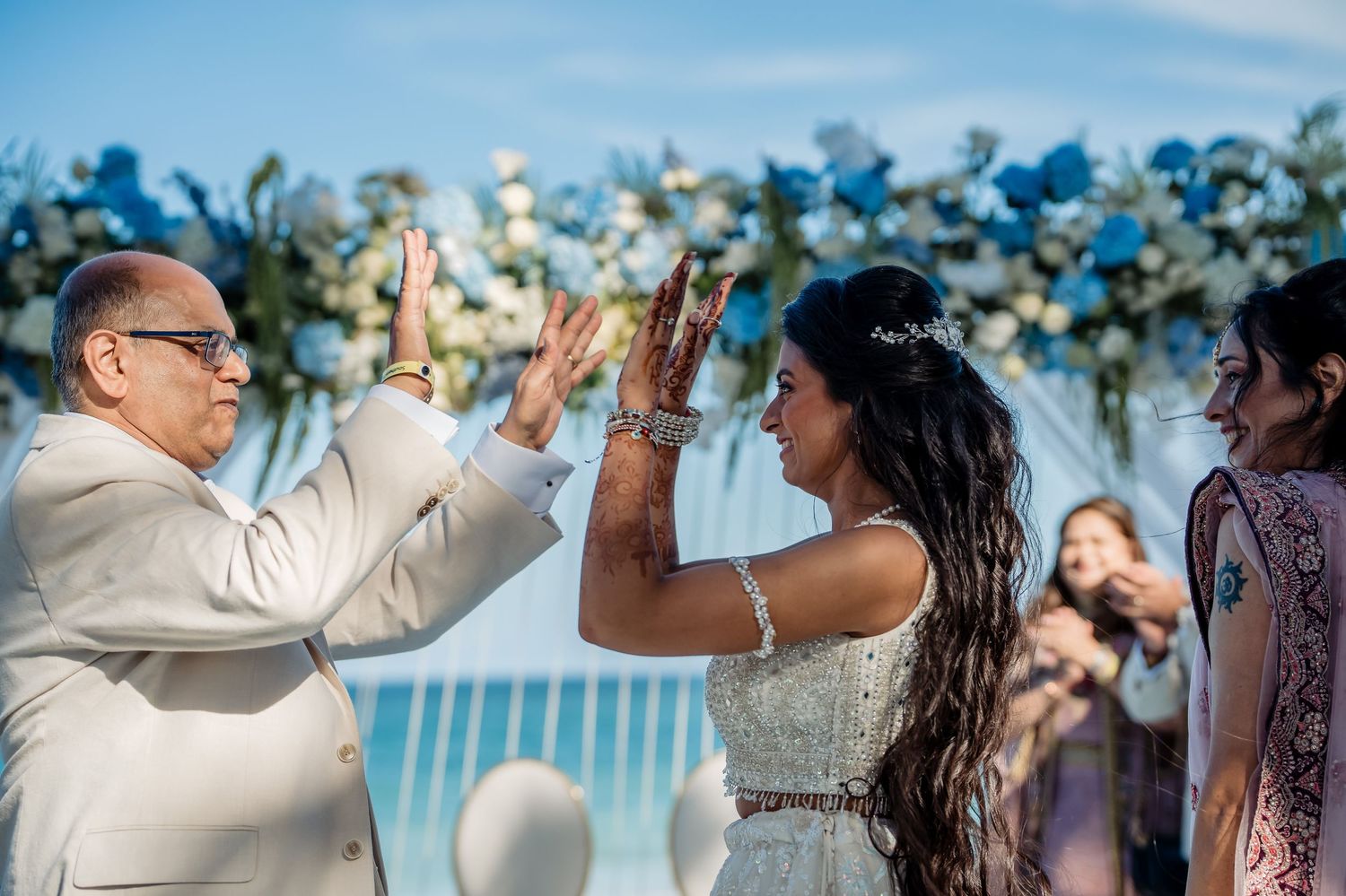 Celebratory high-five moment during beach wedding ceremony with floral arch.