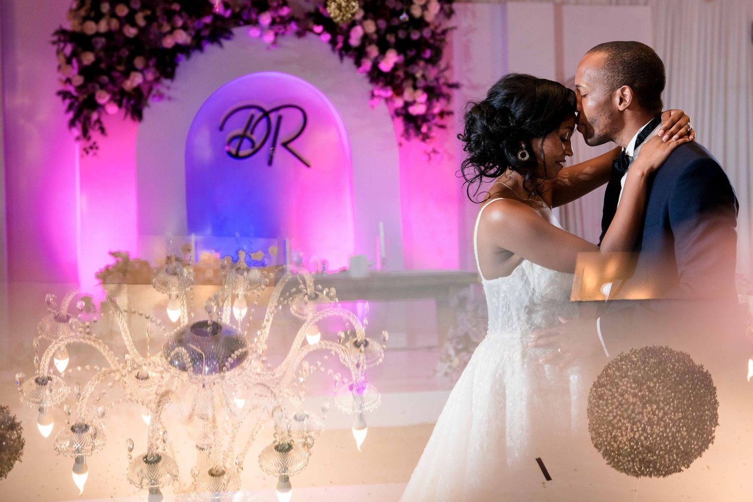 Elegant wedding reception setup with monogram arch, floral decor, and pink uplighting.