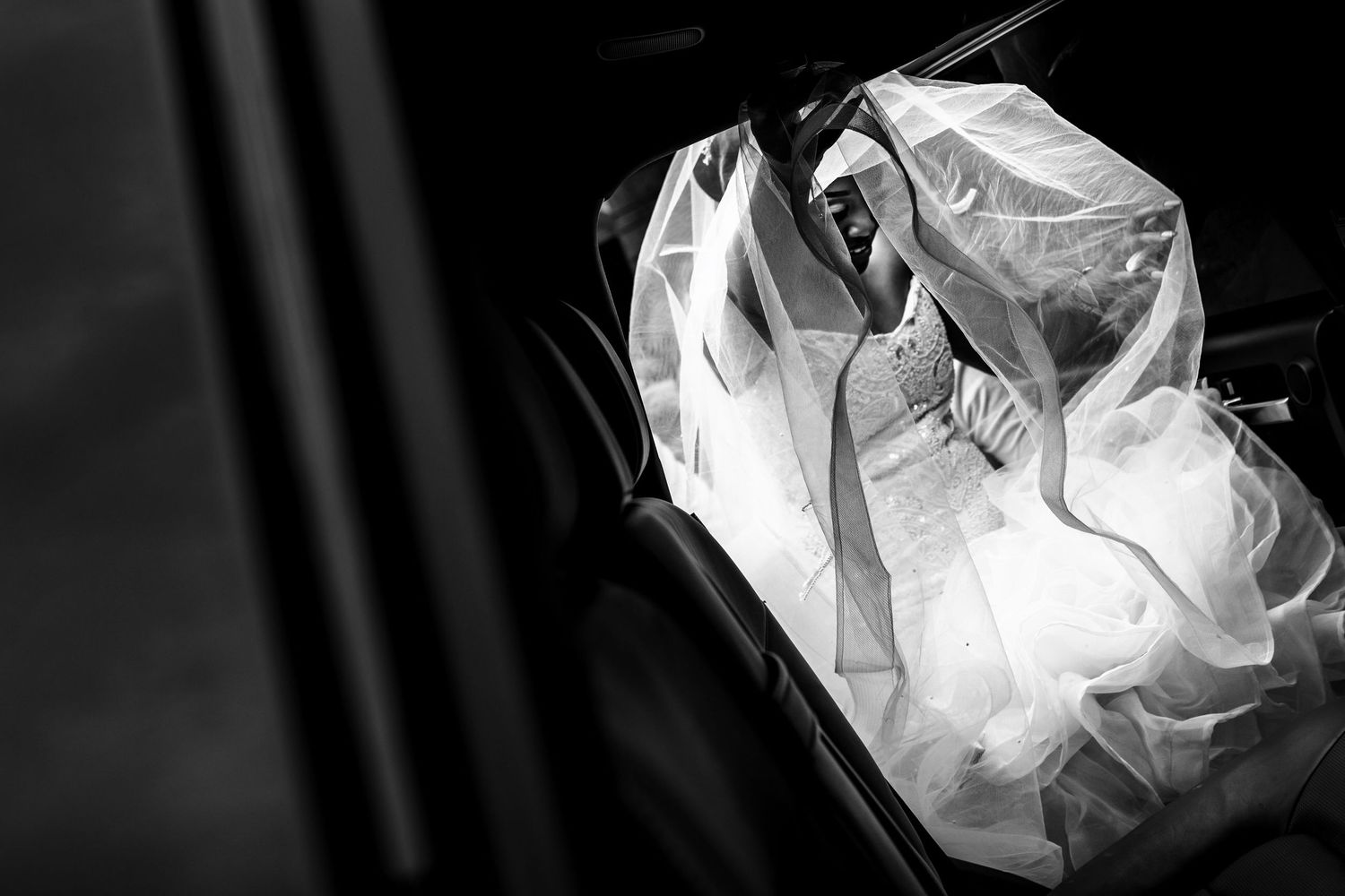 Black and white image of wedding dress hanging in dramatic lighting.