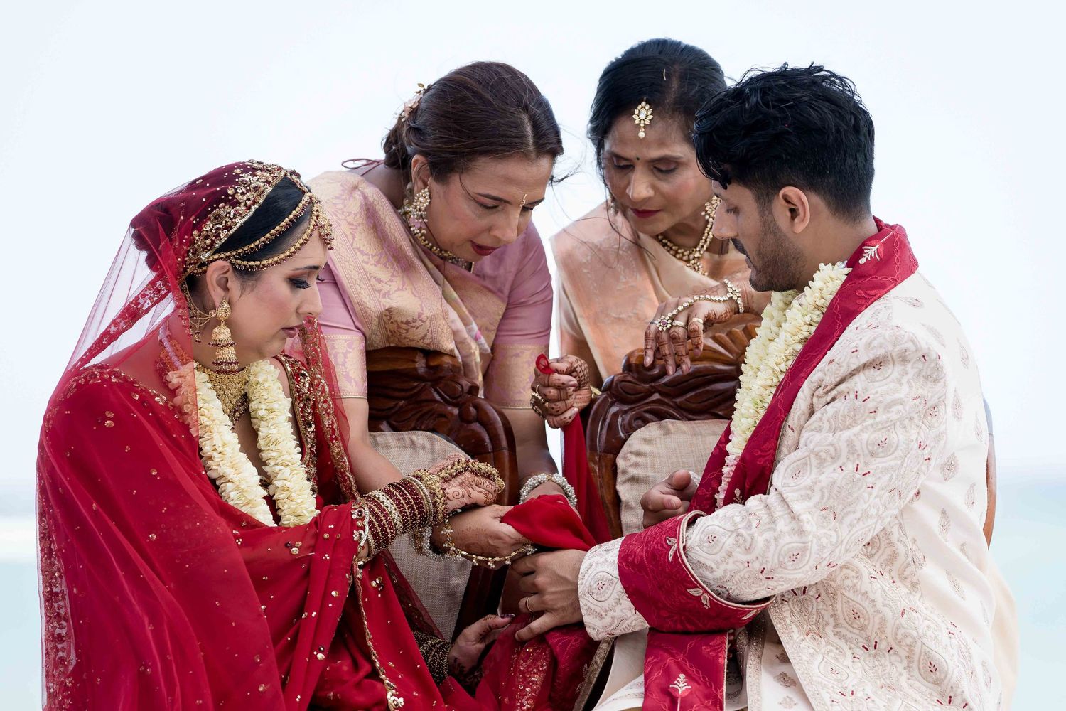 Intimate moment during an Indian wedding ceremony with participants in traditional red and cream attire.