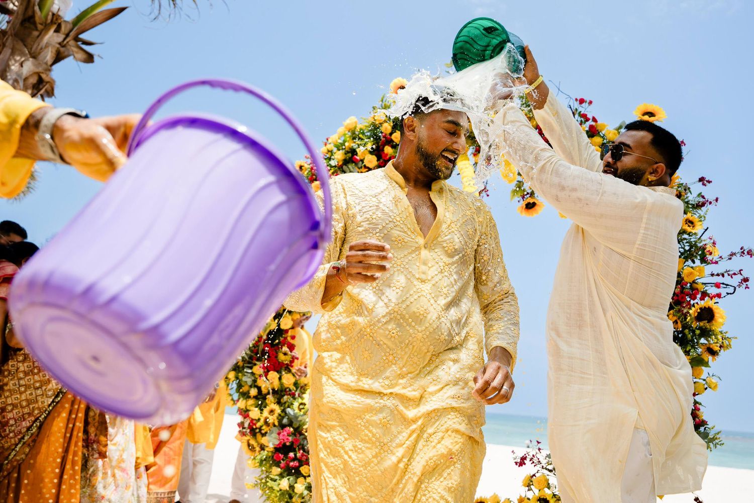 Couple in wedding attire dance joyfully under purple and orange streamers at an outdoor celebration.