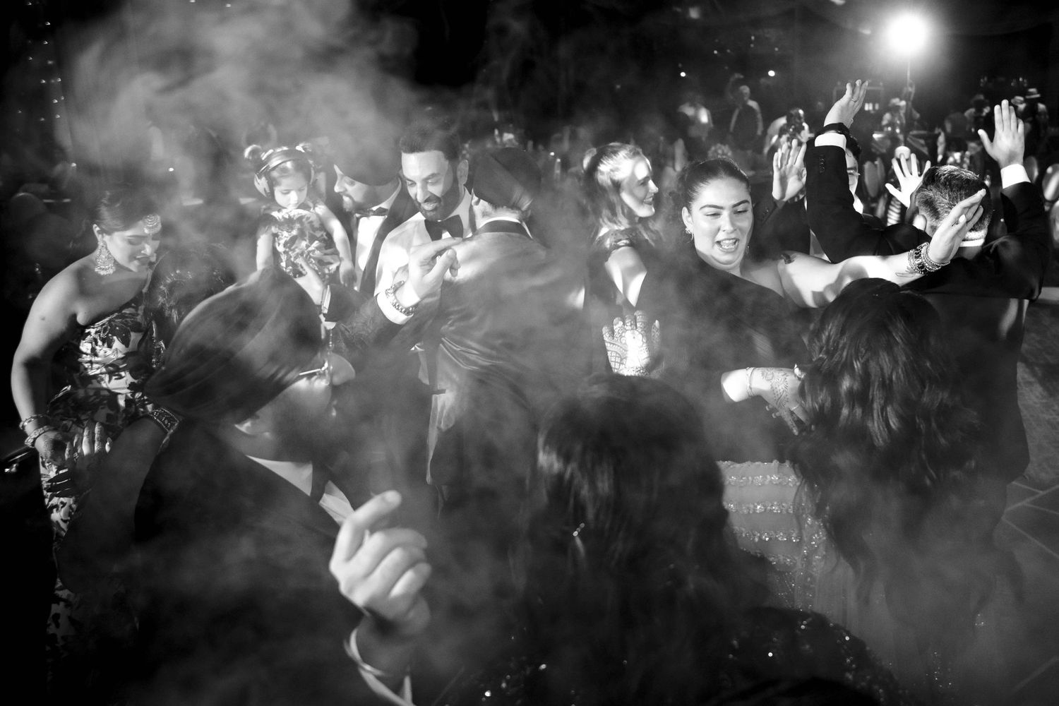 Wedding guests dancing energetically in a black and white photo filled with atmospheric smoke effects.