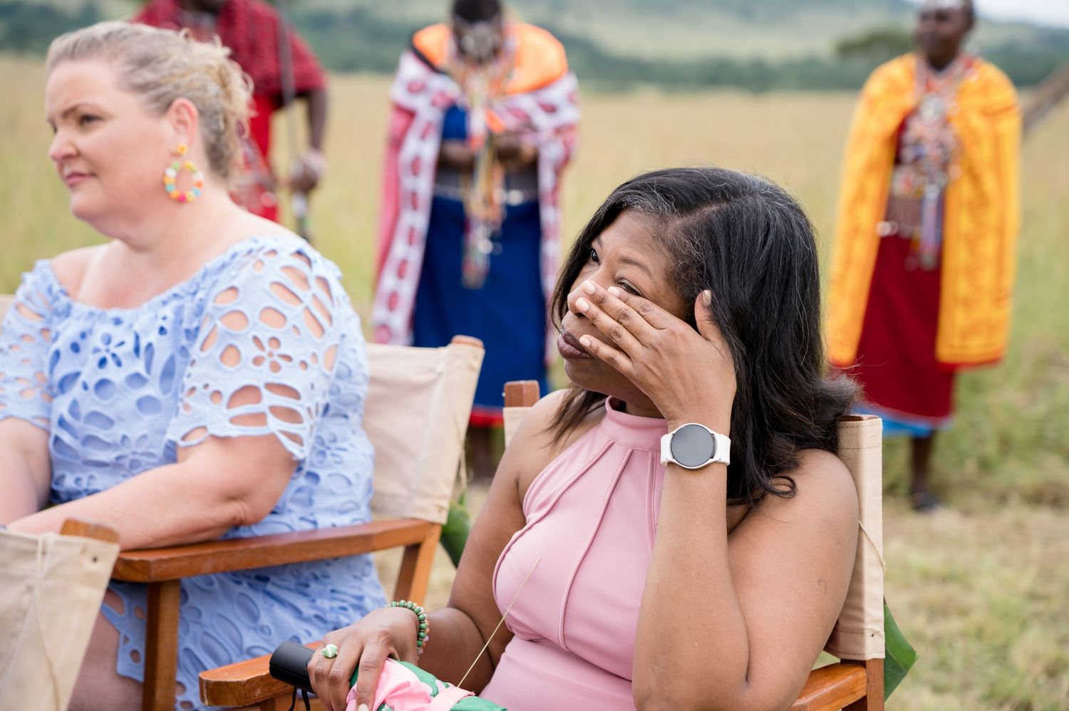 Wedding guest in pink dress covers face with emotion during ceremony.