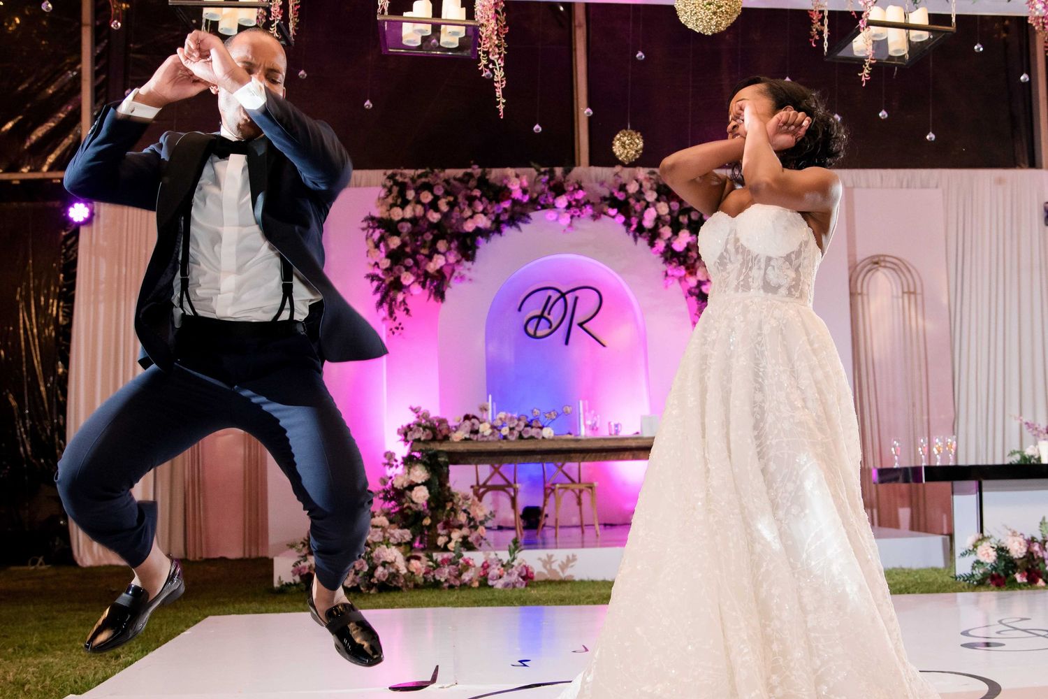 Playful wedding dance moment with jumping groom on decorated reception dance floor.