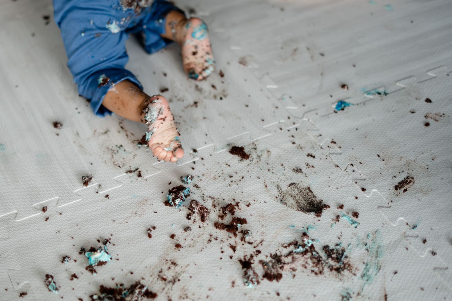 Overhead view of scattered dirt and turquoise paint on floor with blue jean-clad legs visible.