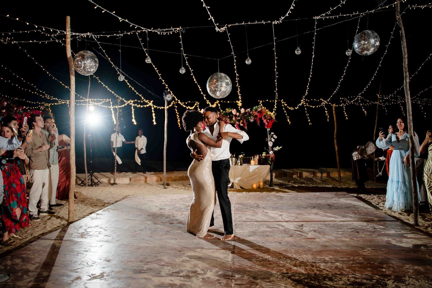 Couples dancing under string lights at an outdoor evening wedding reception on a rustic wooden dance floor.