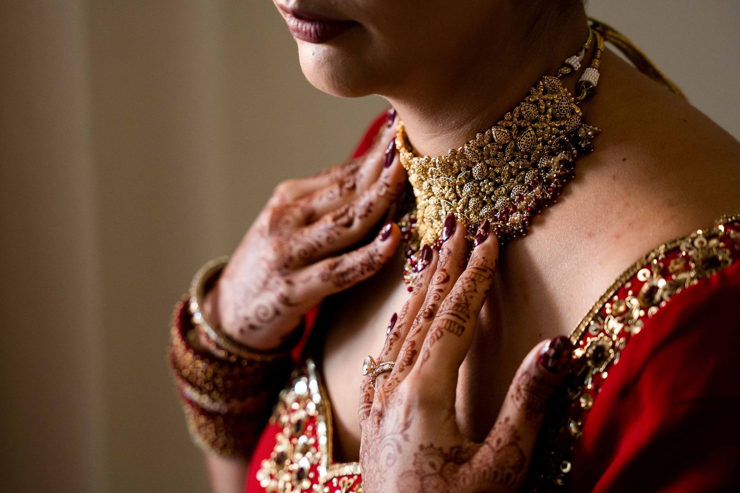 Close up of traditional Indian bridal jewelry and henna adorned hands against a red outfit.