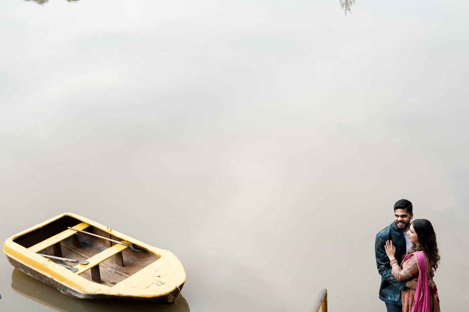 A couple embraces near a small boat on a misty lake creating a romantic atmosphere.