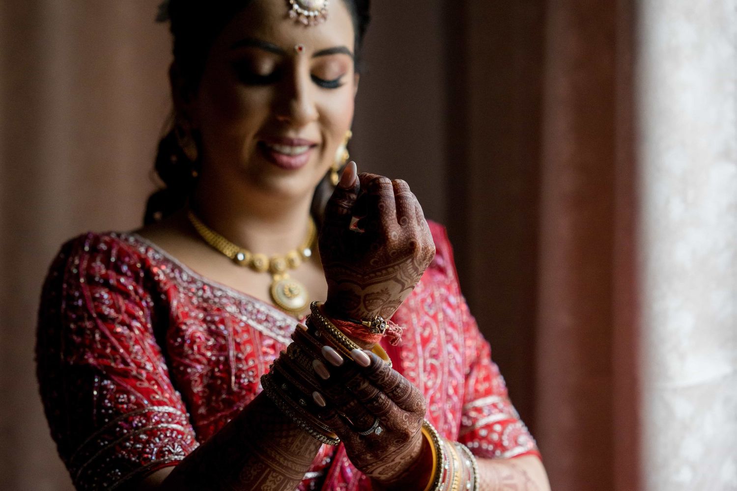 Traditional Indian bridal details featuring red embroidered dress and gold jewelry in natural light.