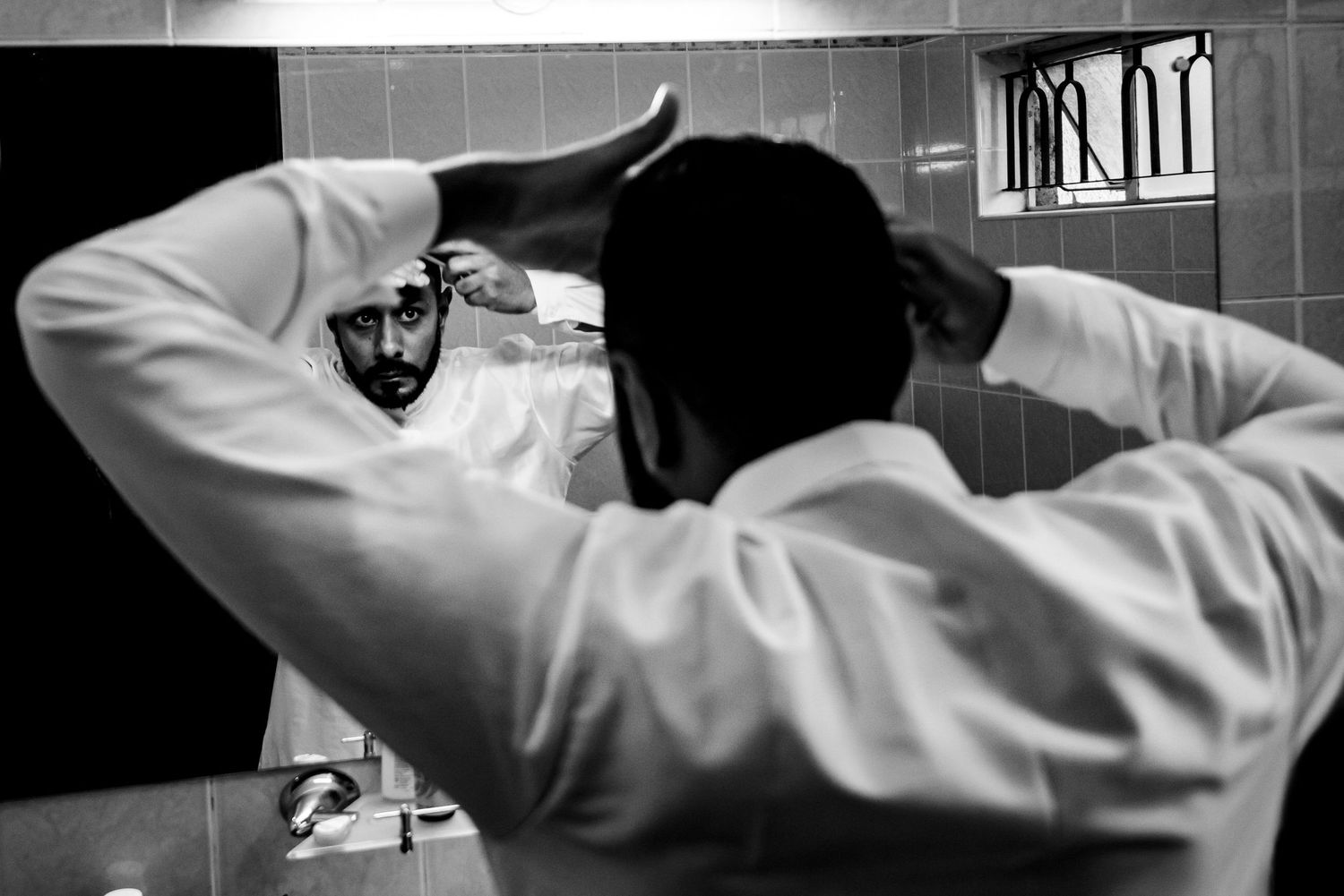Black and white image of someone adjusting their attire in a mirror.
