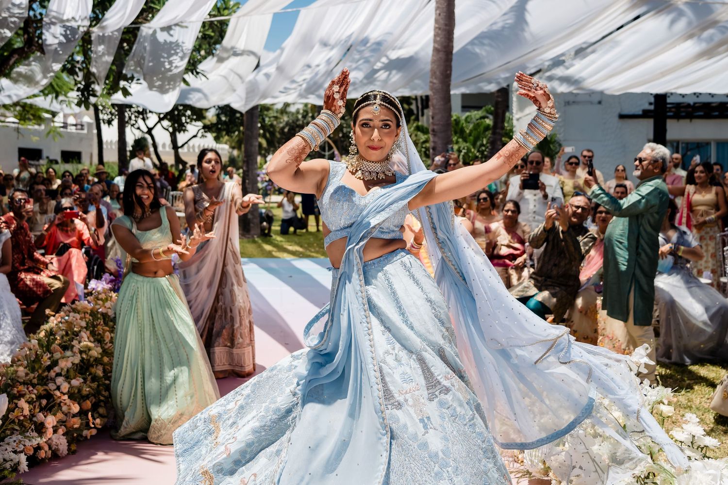 Joyful dancing at outdoor wedding reception under white tent and floral decorations.