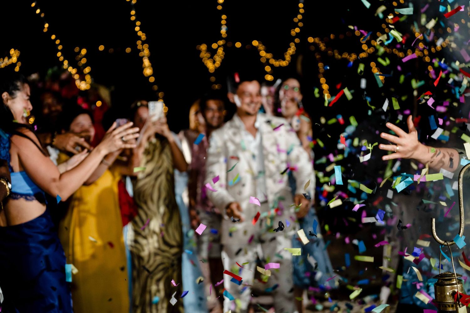 People dancing and celebrating at a party with colorful confetti falling from above in a dimly lit venue.