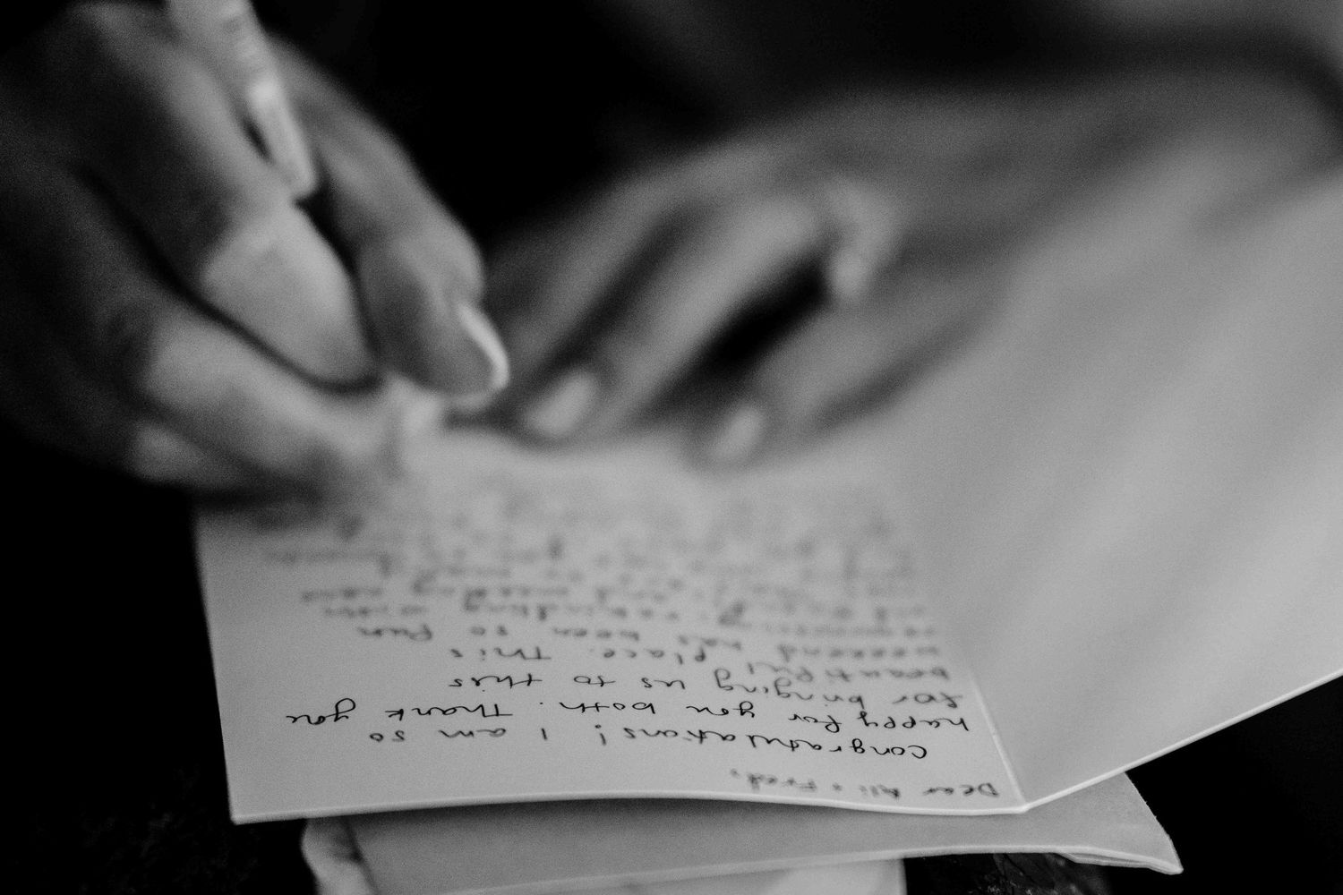 A hand writes with a pen on white paper in black and white, capturing an intimate moment of handwriting.