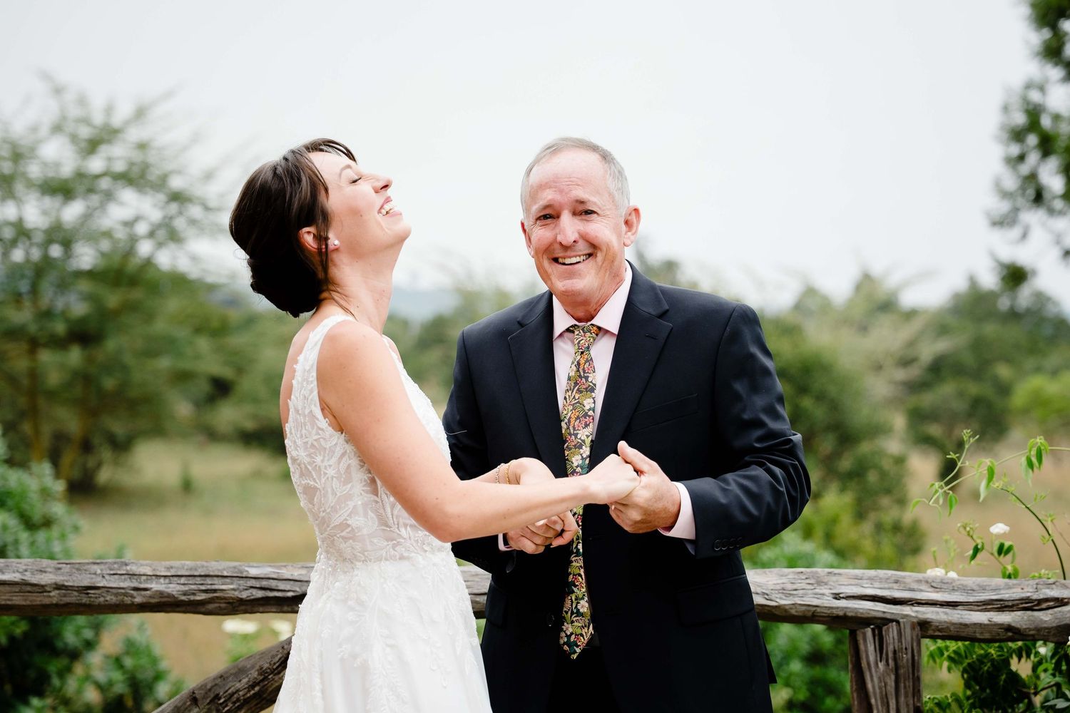 A happy couple shares joyful moments during their outdoor wedding photoshoot on a rustic wooden fence.
