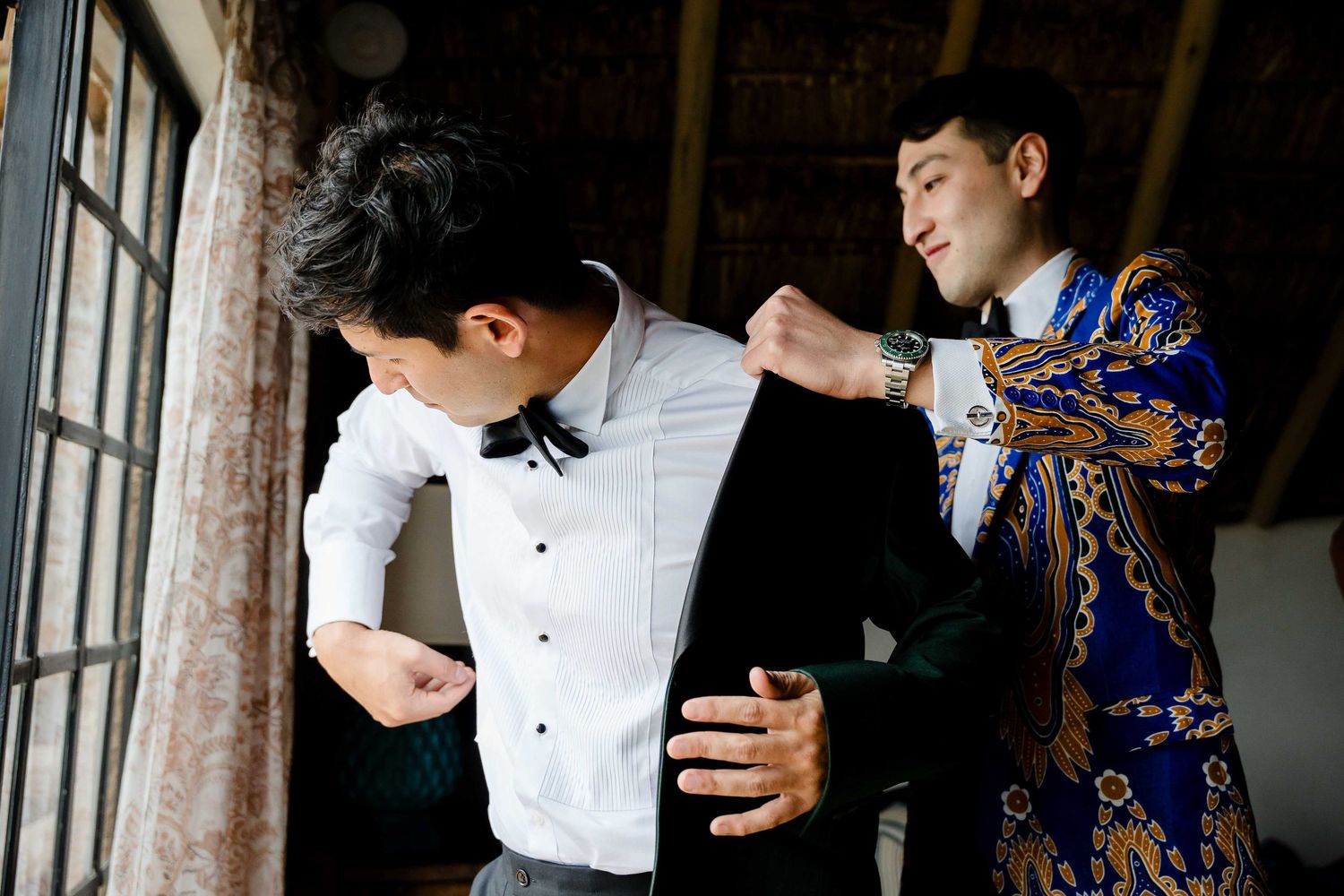 A couple in formal attire dances together in an elegant indoor setting with natural light streaming through windows.